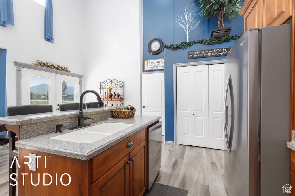 Kitchen with stainless steel appliances, a sink, a high ceiling, brown cabinetry, and light wood finished floors