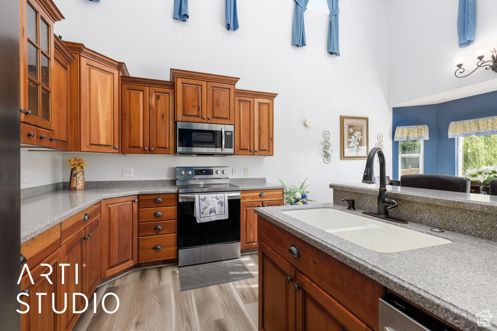 Kitchen with appliances with stainless steel finishes, a sink, a high ceiling, light wood finished floors, and glass insert cabinets
