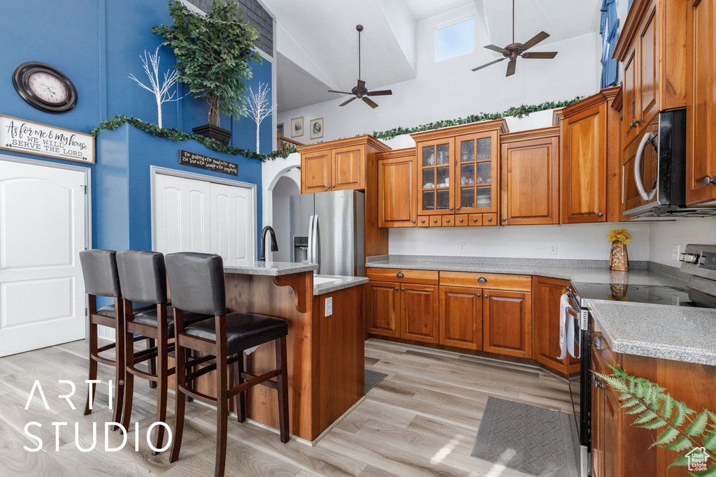 Kitchen with appliances with stainless steel finishes, high vaulted ceiling, a ceiling fan, brown cabinetry, and a breakfast bar area