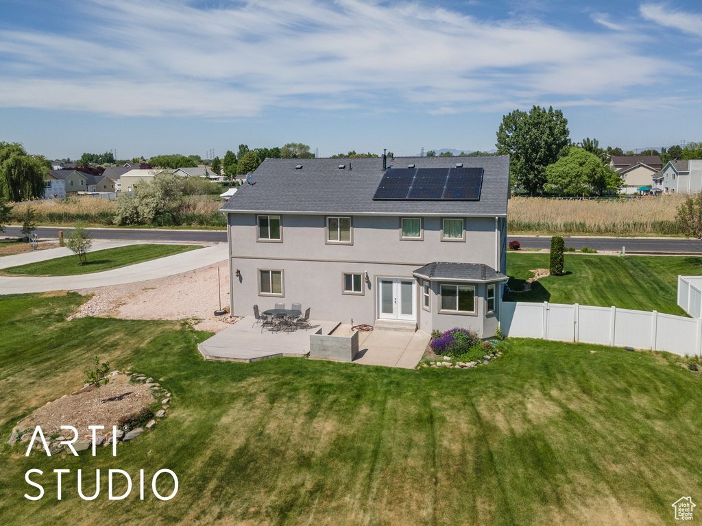 Rear view of property featuring french doors, a patio area, roof mounted solar panels, stucco siding, and roof with shingles