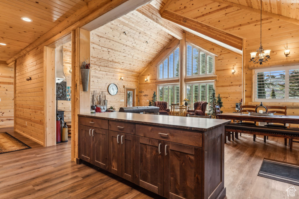 Kitchen with wood ceiling with exposed beams, wood walls, wood finished floors, dark brown cabinetry, and decorative light fixtures