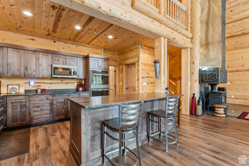 Kitchen with stainless steel appliances, a wood stove, recessed lighting, dark wood-style flooring, and a kitchen bar