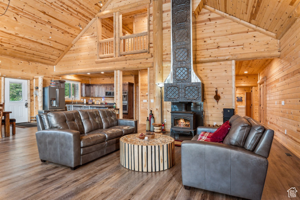 Living room with high vaulted ceiling, wooden ceiling, wooden walls, a wood stove, and wood finished floors