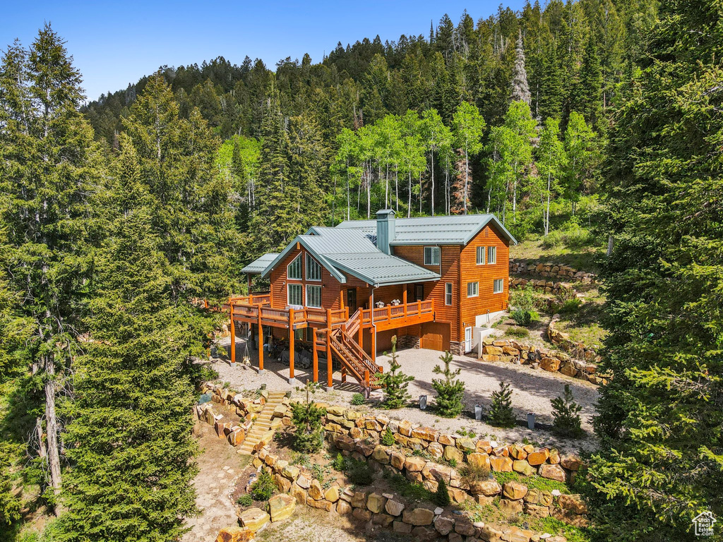 Rear view of house featuring a view of trees, stairs, a garage, a deck, and a chimney