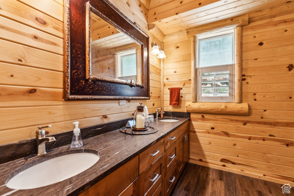 Bathroom with wood walls, double vanity, and wood finished floors