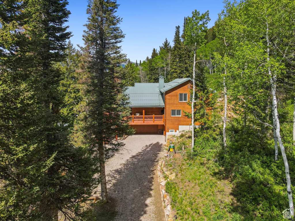 Chalet / cabin with dirt driveway, a wooded view, metal roof, a chimney, and a deck