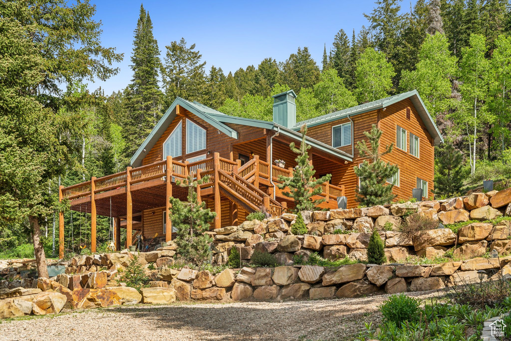 View of home\'s exterior with a wooden deck, a chimney, log veneer siding, and a view of trees