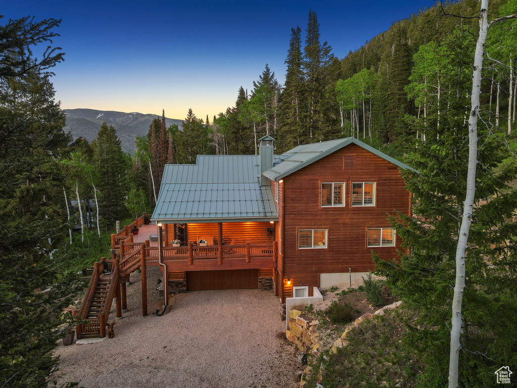 Back of property at dusk featuring driveway, a forest view, metal roof, and a chimney