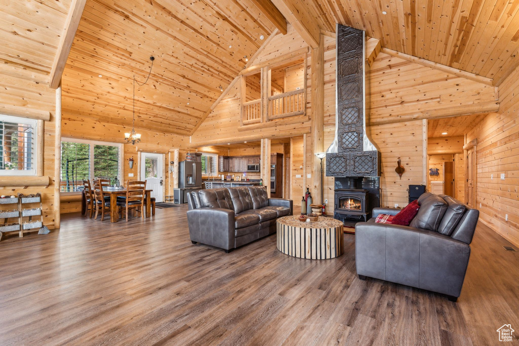 Living room featuring high vaulted ceiling, wooden ceiling with exposed beams, a wood stove, a chandelier, and wood walls