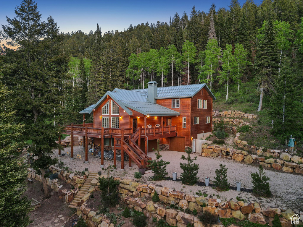 Back of house with a view of trees, driveway, stairway, a deck, and a chimney