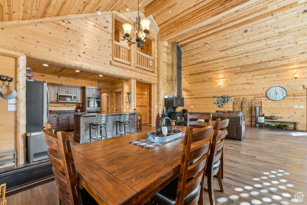 Dining room with wood ceiling, wood walls, light wood-style flooring, high vaulted ceiling, and a chandelier