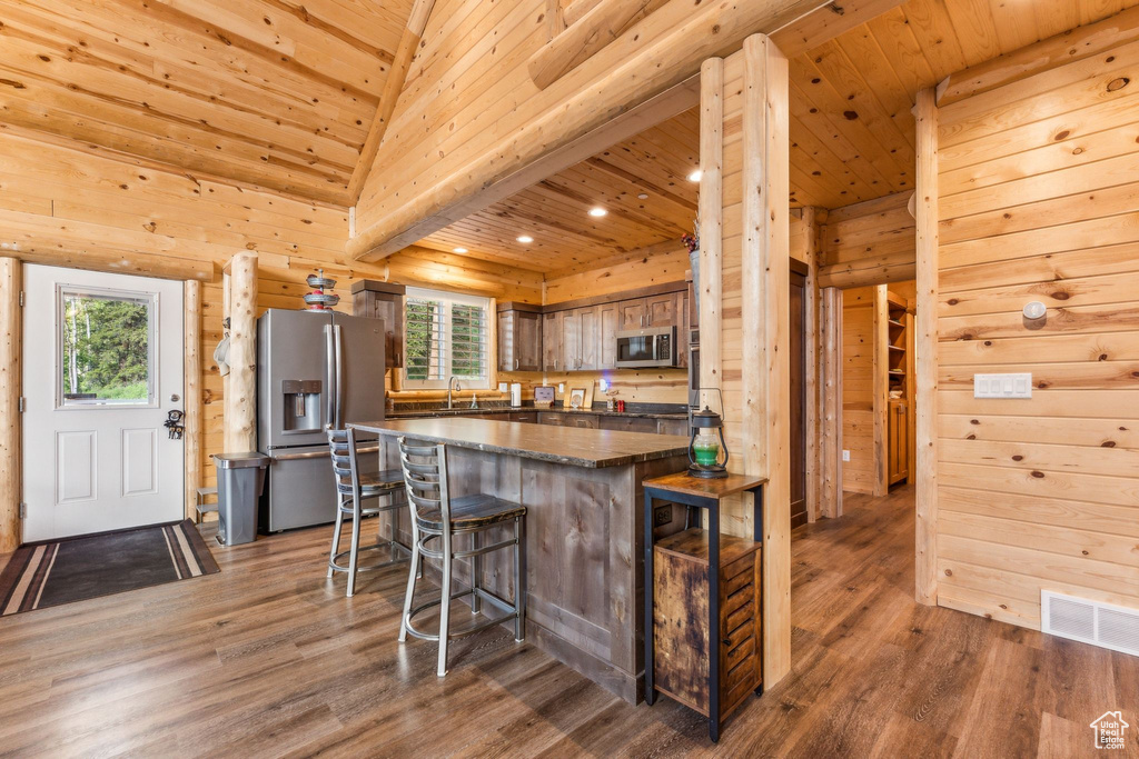 Kitchen featuring appliances with stainless steel finishes, a sink, wood finished floors, a breakfast bar area, and wood ceiling