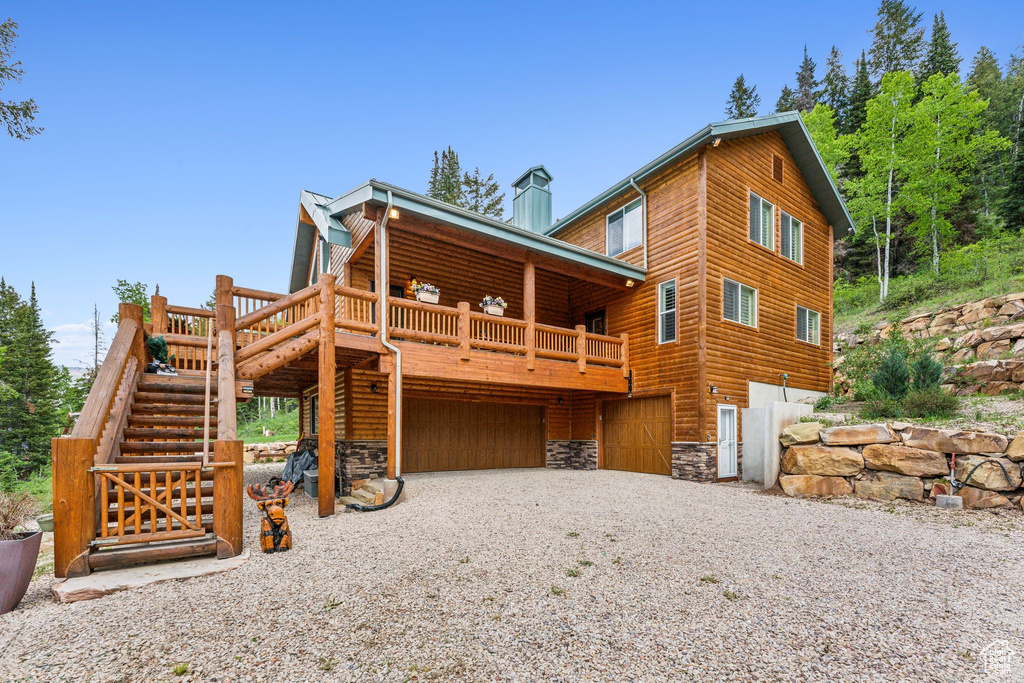 Rear view of house featuring stairs, stone siding, a garage, driveway, and a wooden deck