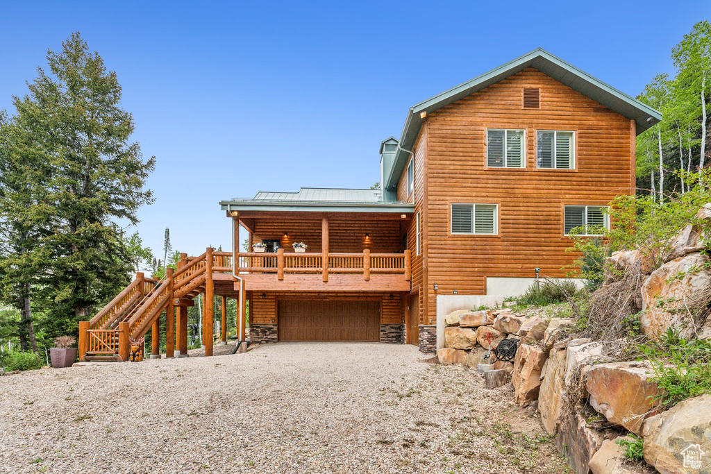 Back of house with an attached garage, metal roof, gravel driveway, and stairs