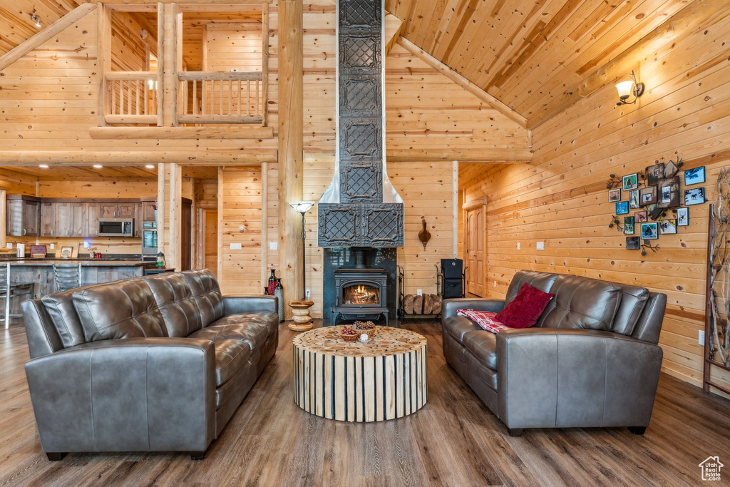 Living area with high vaulted ceiling, wood ceiling, wooden walls, a wood stove, and wood finished floors