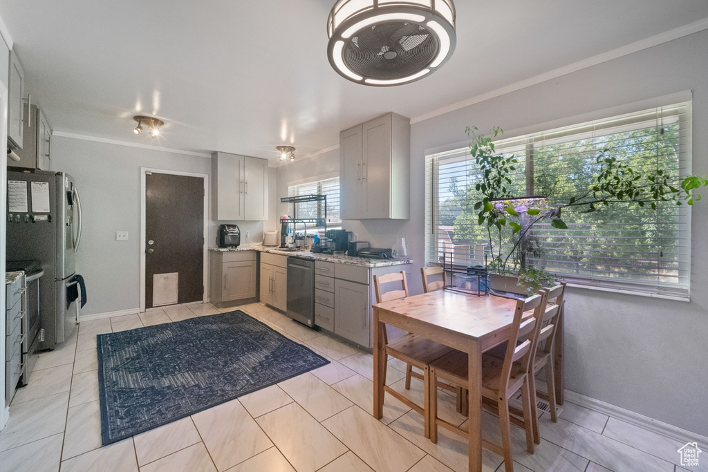 Kitchen with stainless steel appliances, gray cabinetry, ornamental molding, and light stone counters