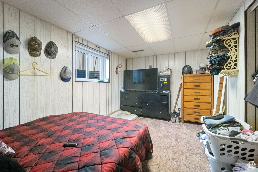 Carpeted bedroom featuring a paneled ceiling and wooden walls