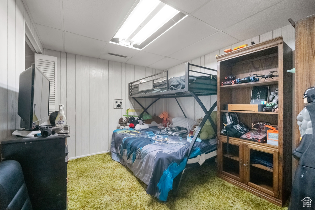 Carpeted bedroom featuring a paneled ceiling and wooden walls
