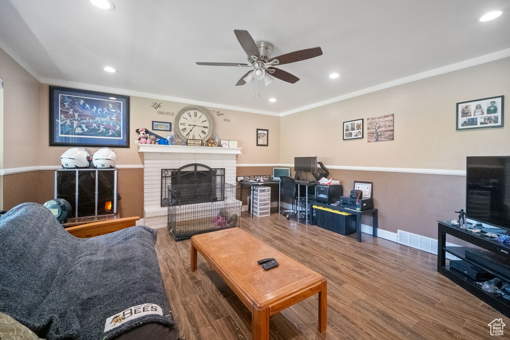 Living room featuring a ceiling fan, recessed lighting, a fireplace, wood finished floors, and crown molding