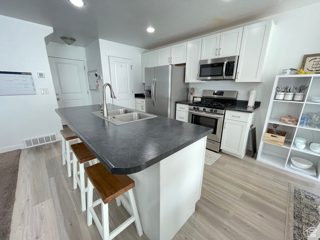 Kitchen with appliances with stainless steel finishes, a sink, dark countertops, light wood finished floors, and recessed lighting