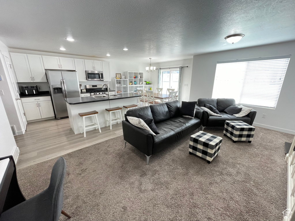 Living room with a textured ceiling, a chandelier, light wood-style floors, recessed lighting, and baseboards