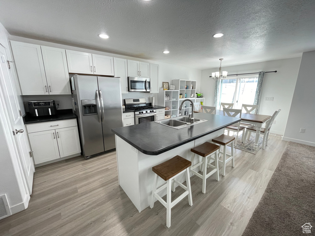 Kitchen with stainless steel appliances, a sink, a chandelier, a breakfast bar, and dark countertops