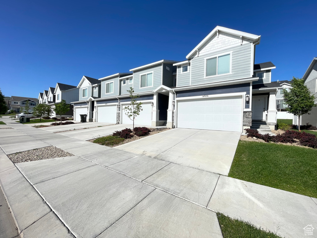 View of front facade with an attached garage, concrete driveway, a residential view, stone siding, and a front lawn