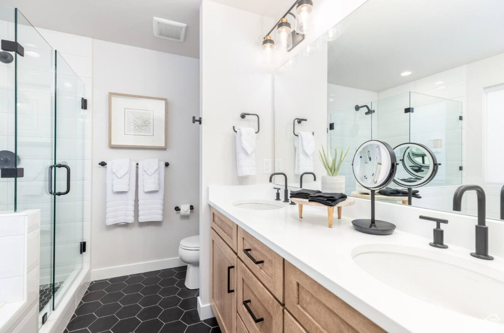 Bathroom featuring double vanity, a stall shower, toilet, baseboards, and tile patterned floors