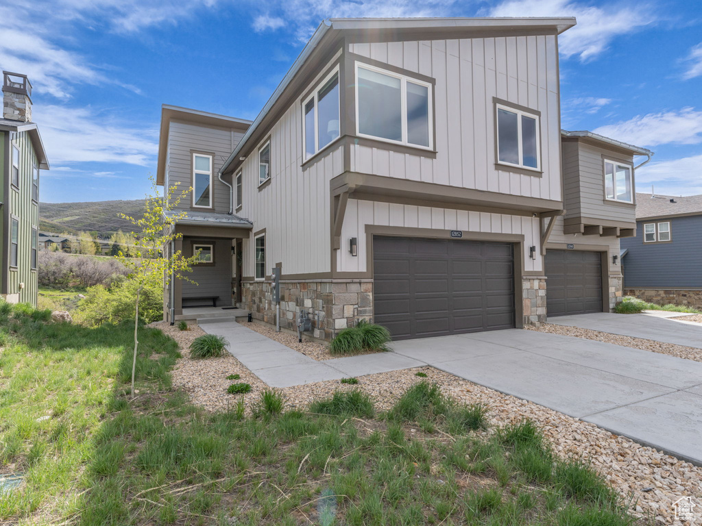 View of front facade featuring stone siding, board and batten siding, a garage, and concrete driveway