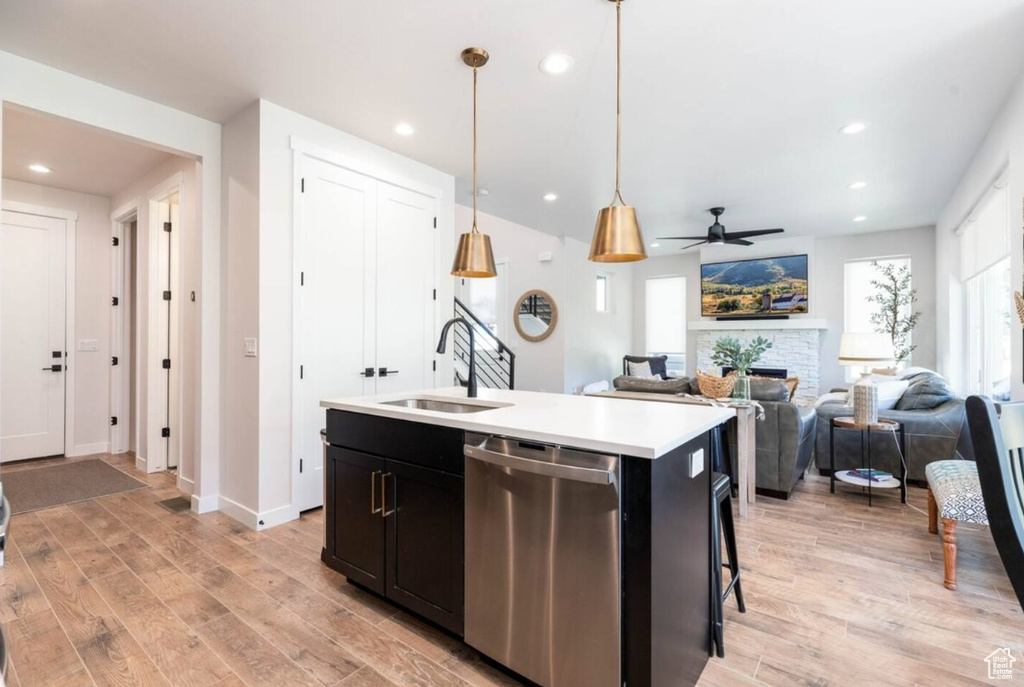 Kitchen with stainless steel dishwasher, a sink, light wood-type flooring, light countertops, and a kitchen island with sink