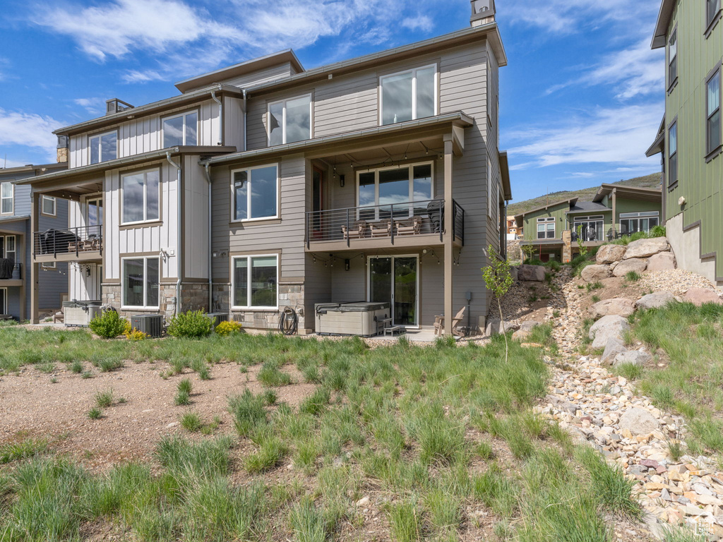Rear view of property featuring a chimney, a balcony, central air condition unit, and a hot tub