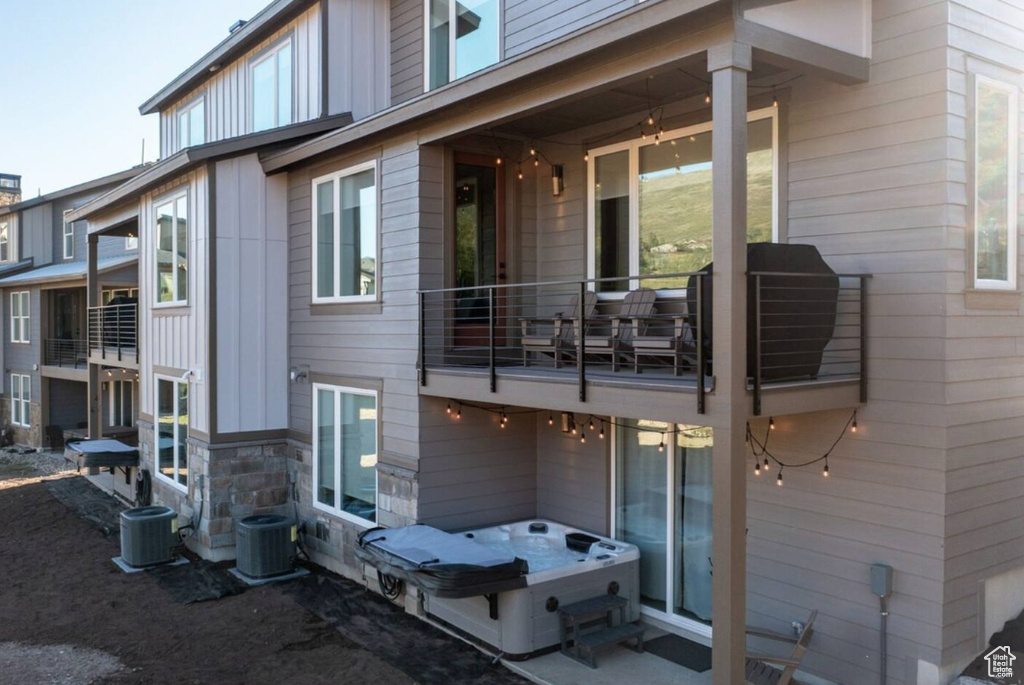 Rear view of property featuring a balcony, central AC, and stone siding