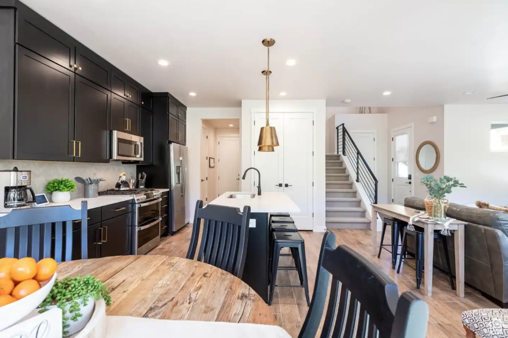 Kitchen with appliances with stainless steel finishes, a sink, light countertops, a kitchen breakfast bar, and recessed lighting