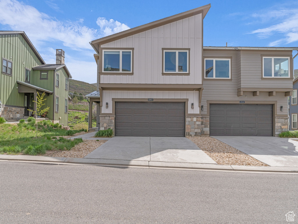 View of front of home with stone siding, an attached garage, driveway, and board and batten siding