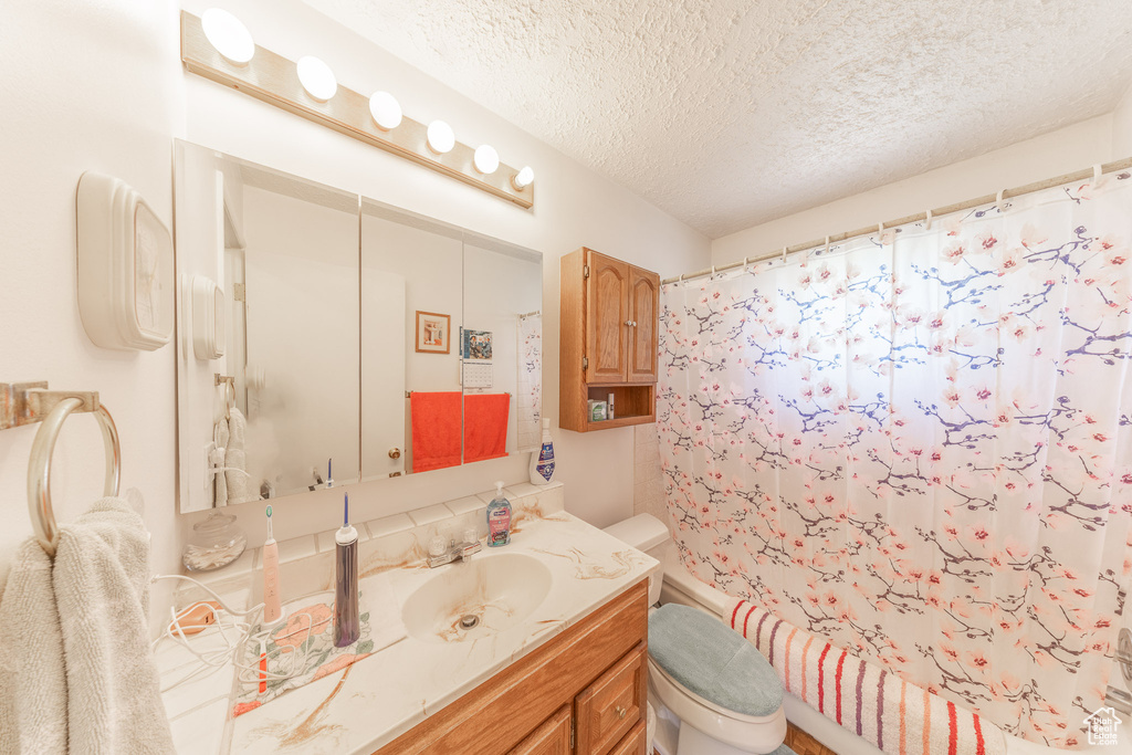 Full bath with toilet, vanity, a textured ceiling, and shower / bath combination with curtain