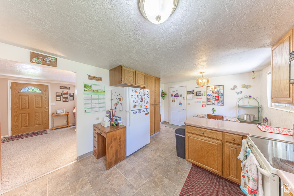 Kitchen with freestanding refrigerator, a peninsula, electric stove, light countertops, and a textured ceiling
