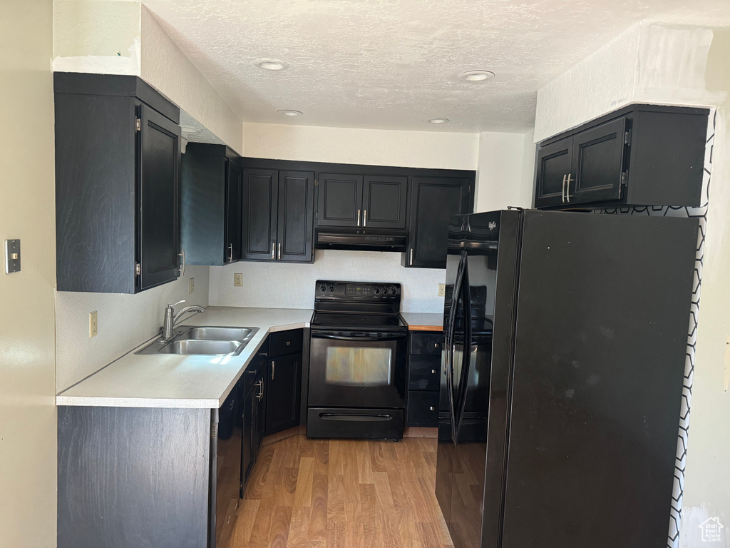 Kitchen with black appliances, a sink, under cabinet range hood, light wood-type flooring, and light countertops