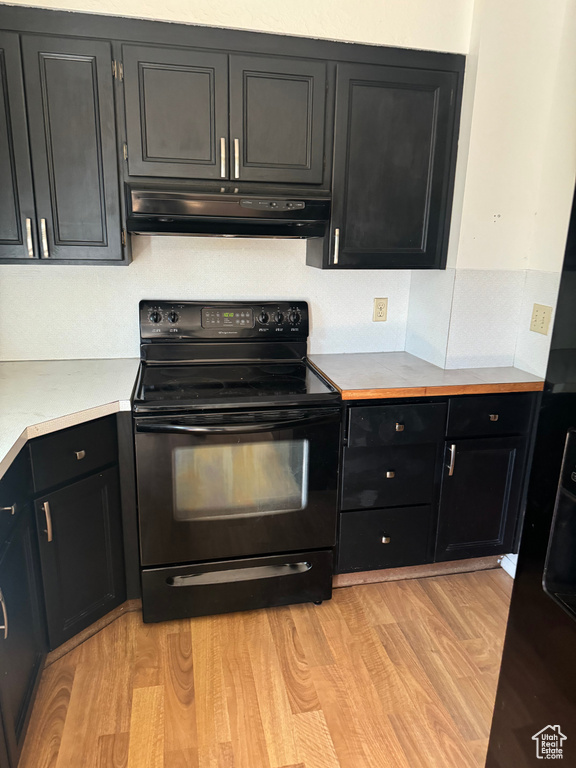 Kitchen with black electric range oven, exhaust hood, dark cabinetry, light countertops, and light wood-style flooring