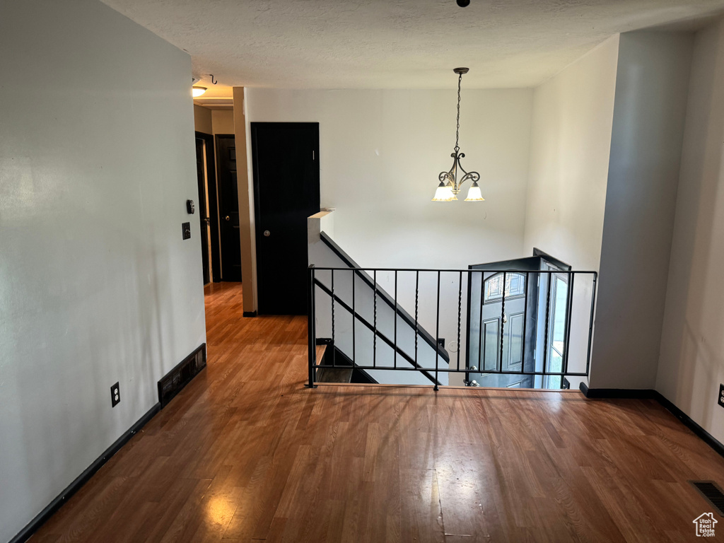 Empty room with wood finished floors, a chandelier, and baseboards