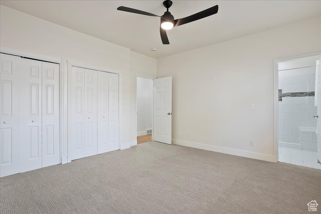 Unfurnished bedroom with light colored carpet, two closets, connected bathroom, baseboards, and ceiling fan