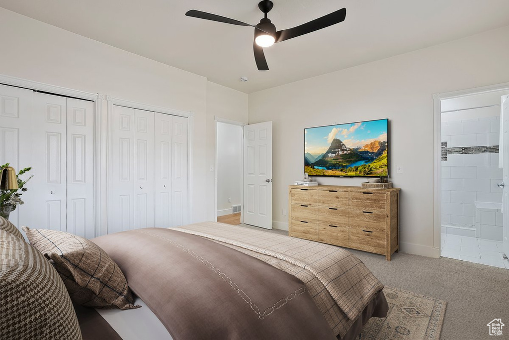 Bedroom featuring two closets, light colored carpet, ensuite bath, baseboards, and ceiling fan