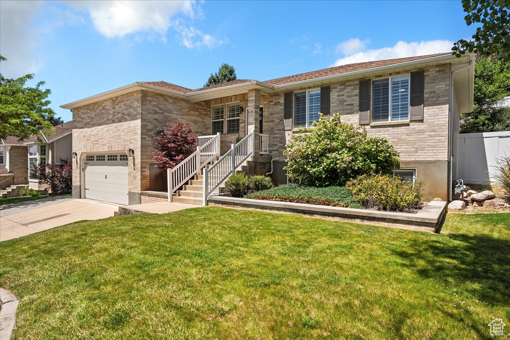 View of front of property with driveway, an attached garage, a front lawn, and brick siding