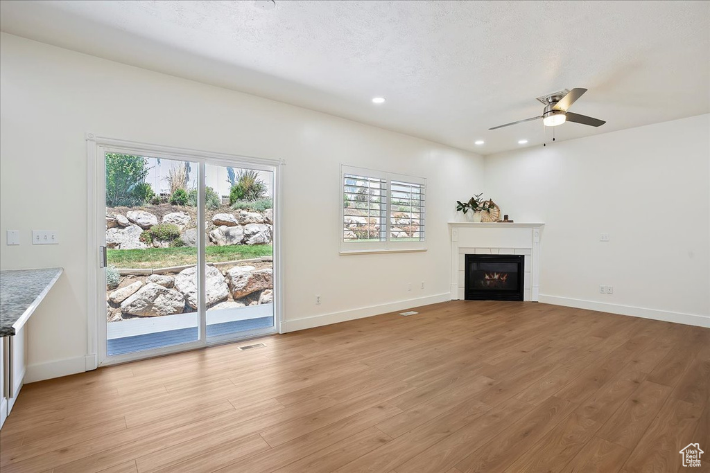 Unfurnished living room with light wood-style flooring, a ceiling fan, healthy amount of natural light, a tiled fireplace, and recessed lighting