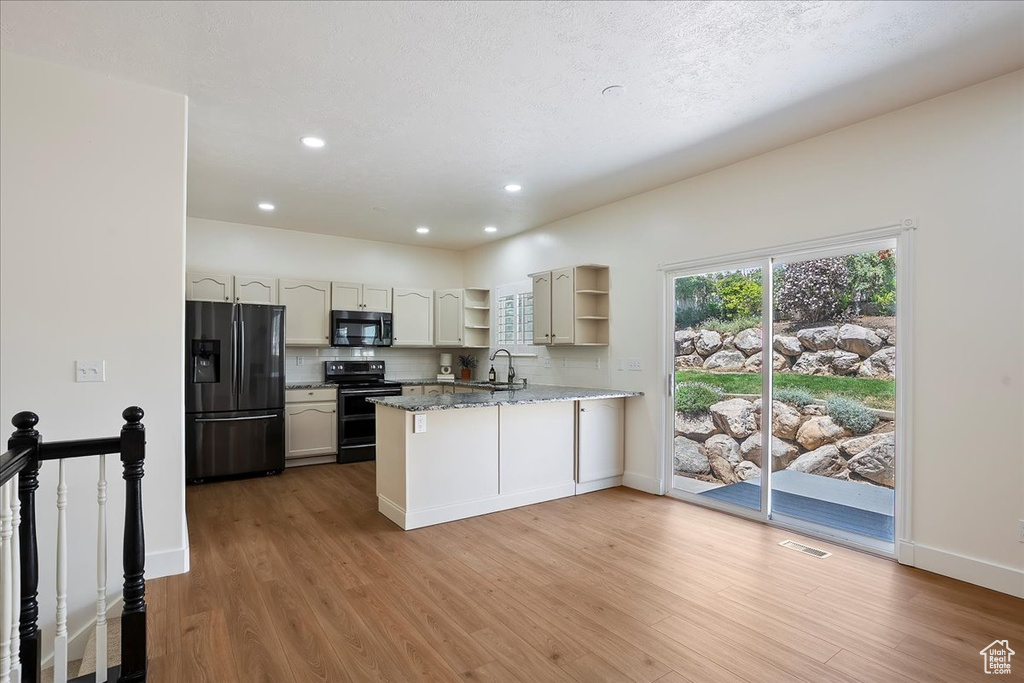 Kitchen with refrigerator with ice dispenser, range, a sink, open shelves, and a peninsula