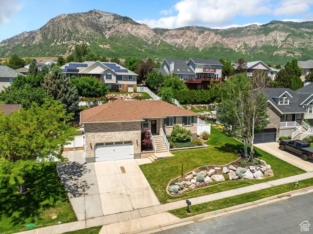 View of front of home with concrete driveway, a residential view, a mountain view, stairs, and a front lawn