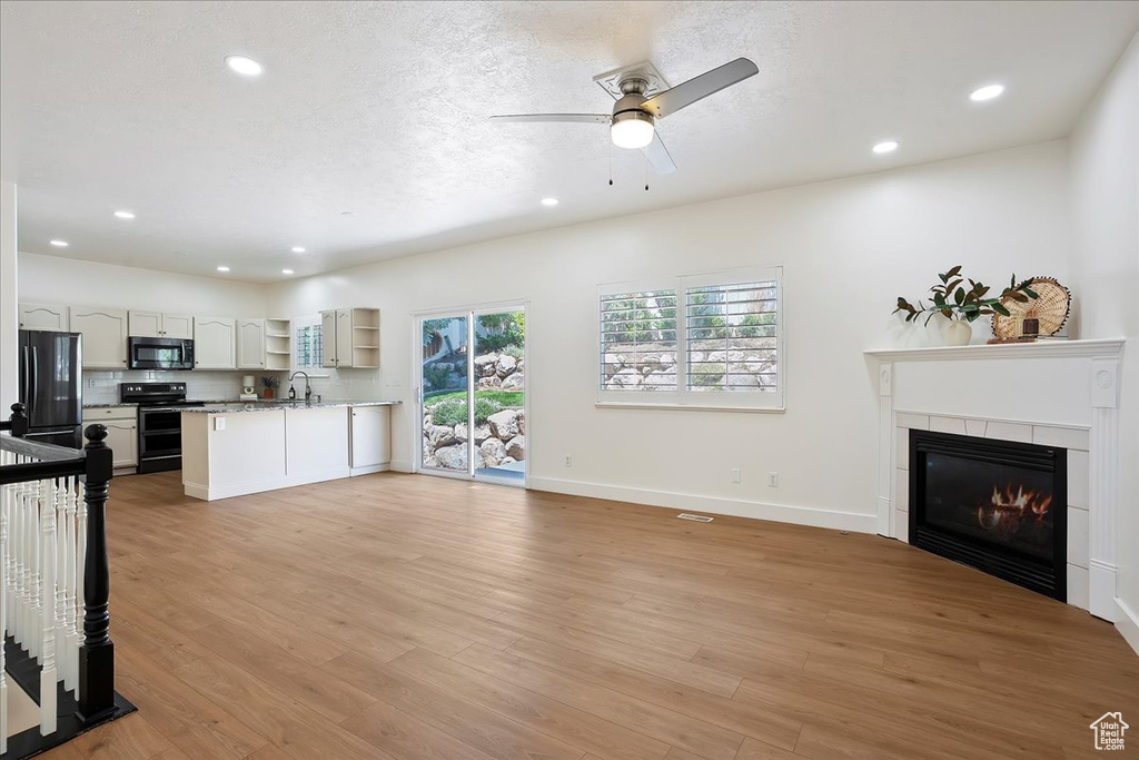 Unfurnished living room with recessed lighting, ceiling fan, a tile fireplace, light wood-style floors, and baseboards