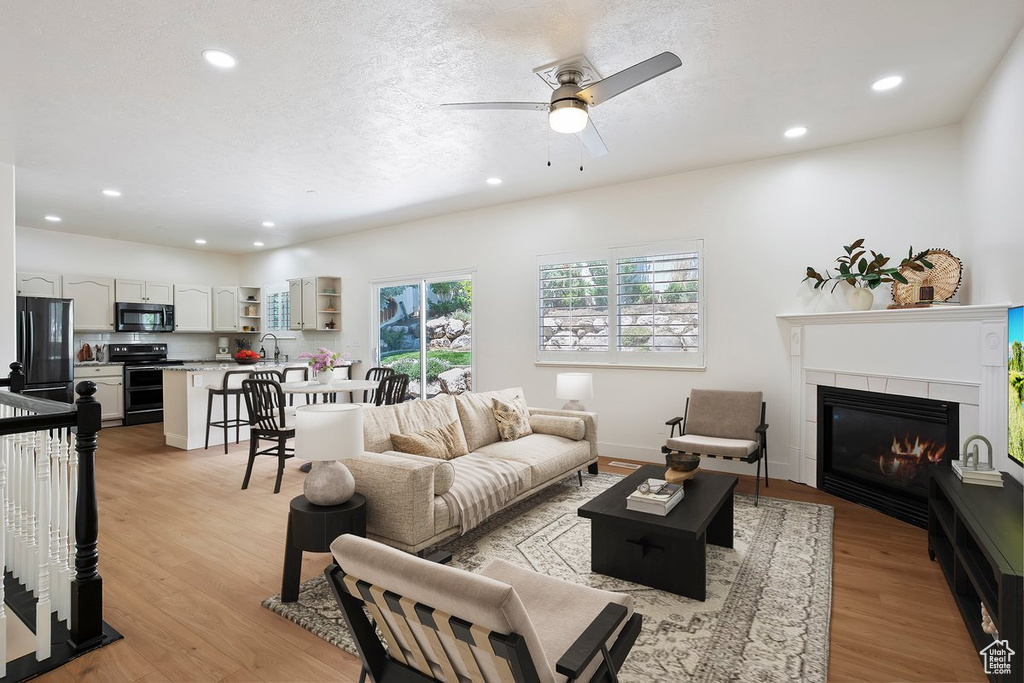Living area featuring recessed lighting, light wood-type flooring, ceiling fan, a fireplace, and baseboards