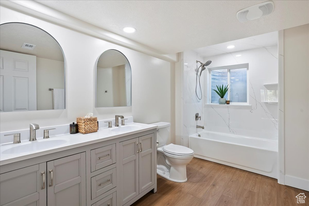 Bathroom with double vanity, toilet, shower / bathtub combination, wood finished floors, and recessed lighting