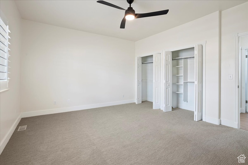 Unfurnished bedroom featuring light carpet, multiple closets, and baseboards