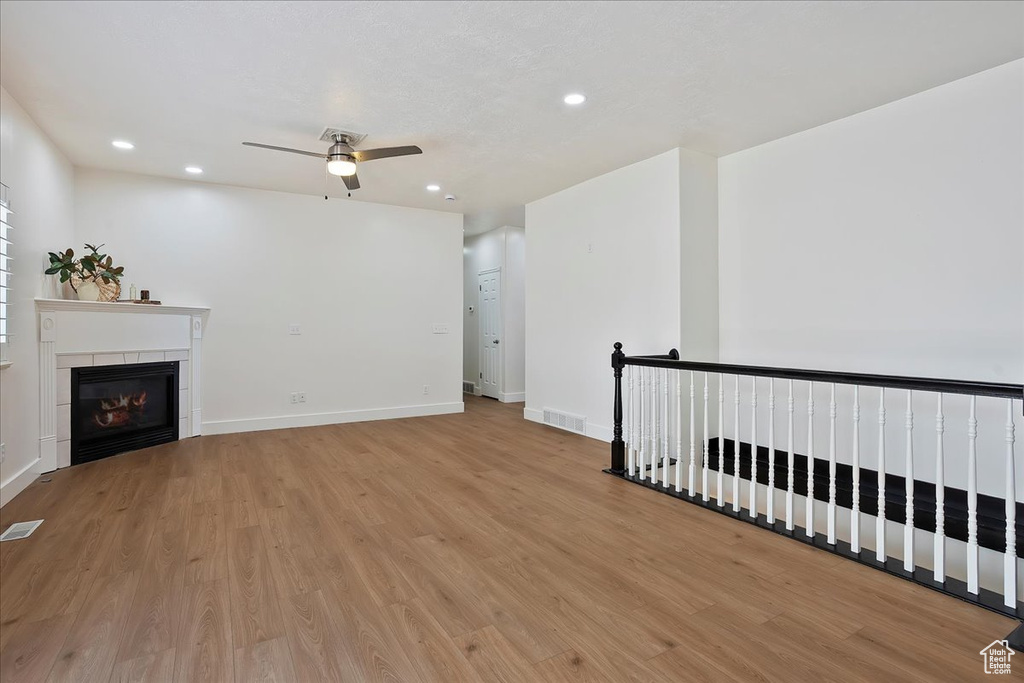Unfurnished living room with a ceiling fan, light wood-type flooring, recessed lighting, a tiled fireplace, and baseboards
